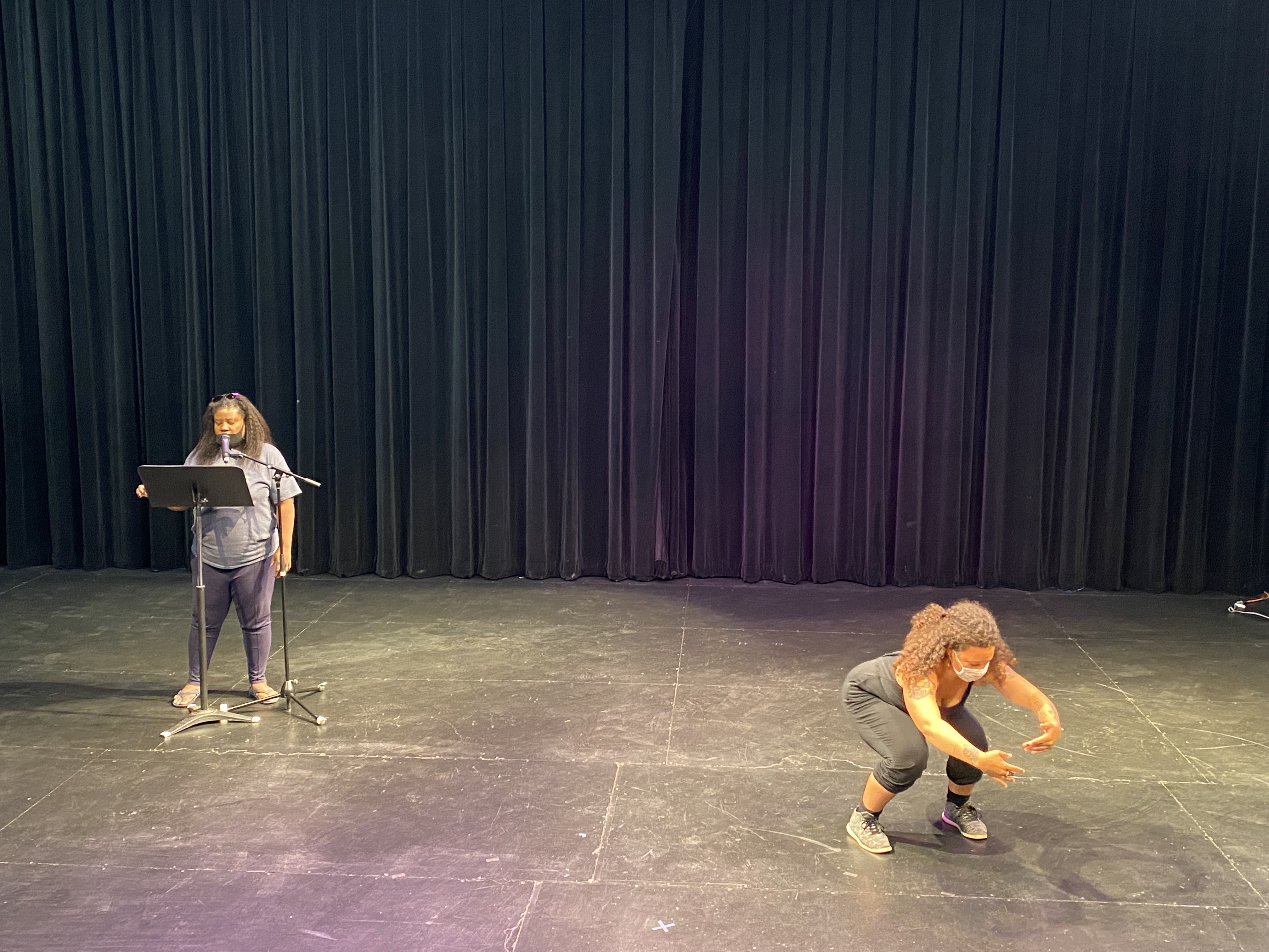 actor Shanda Williams on left at mic & music stand, stands & recites while on right dancer Isadora Snapp crouches with arms extended in semi circle onstage at LNT